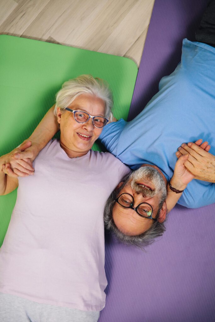 elderly couple laying on the ground on coloured gym mats and holding hands